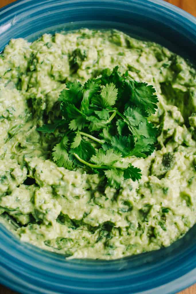 blue bowl of bright green guacamole topped with cilantro