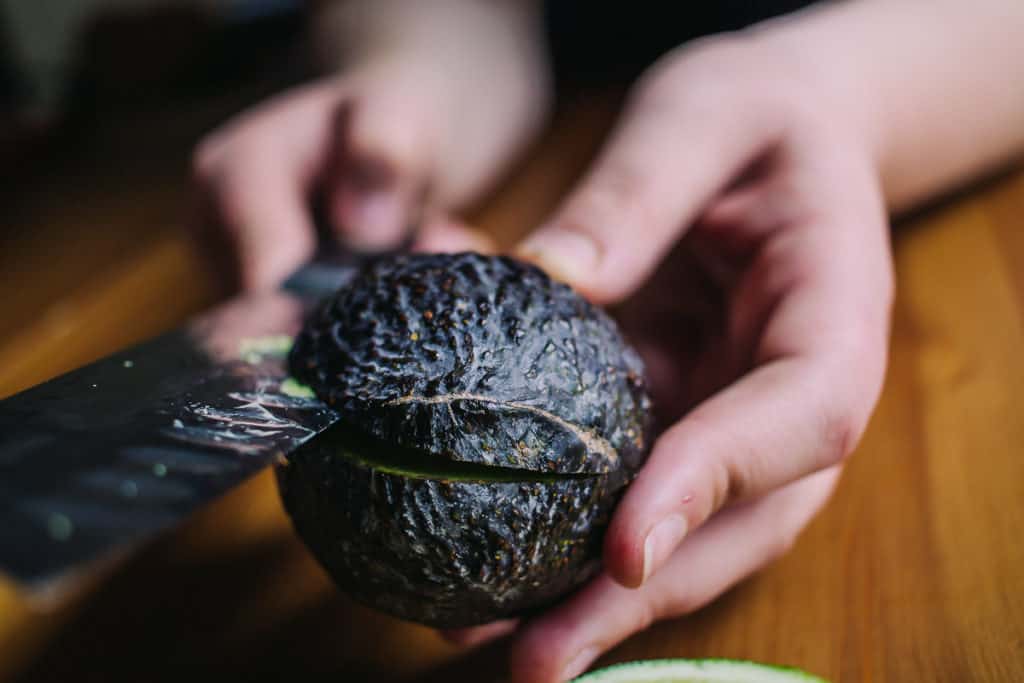 two hands holding an avocado and cutting it with a sharp knife