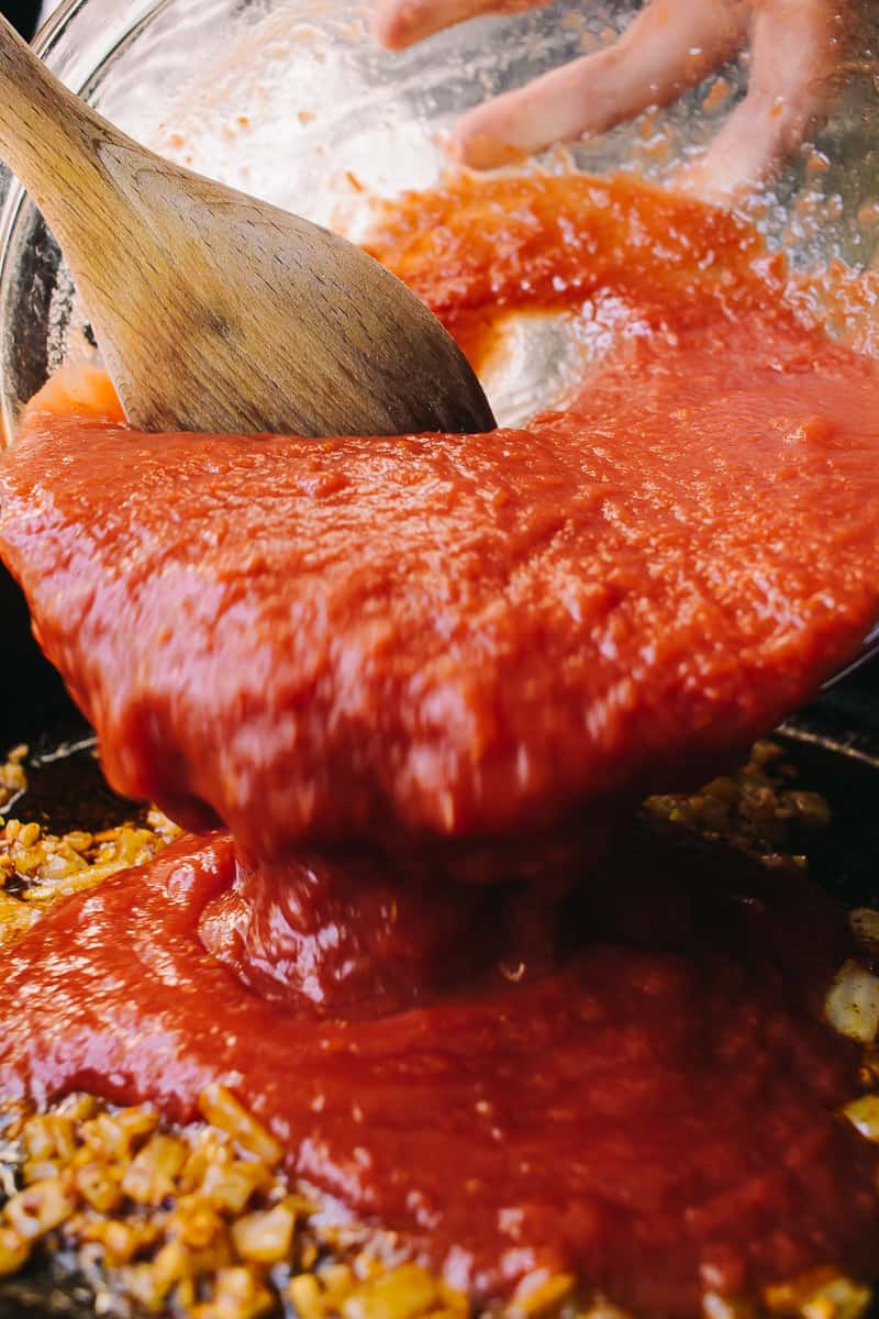 adding crushed tomatoes to a skillet