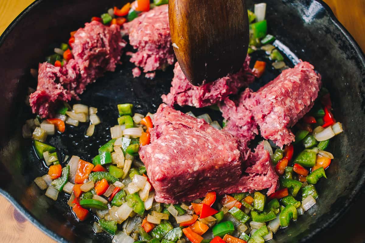 raw ground beef in a skillet with peppers and onions