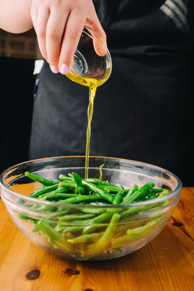 adding olive oil dressing to green beans