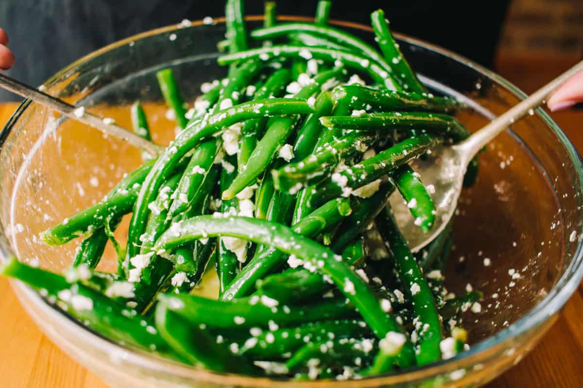 tossing green bean salad with feta cheese crumbles