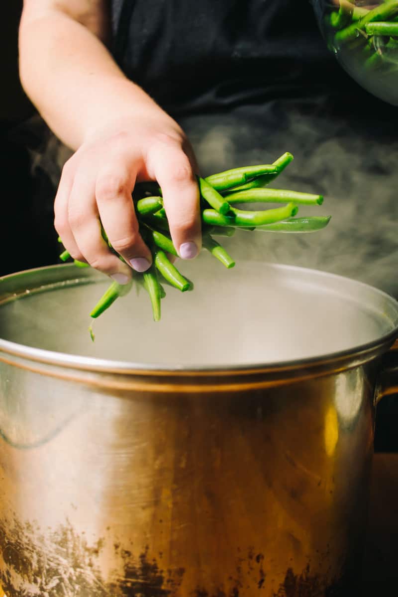hand putting green beans into a pot of boiling water