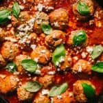 lamb meatballs in marinara sauce with feta cheese and basil in a cast iron skillet