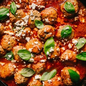 lamb meatballs in marinara sauce with feta cheese and basil in a cast iron skillet
