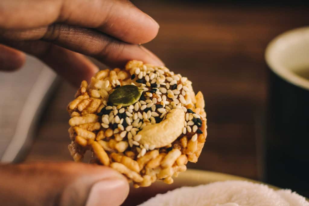 man's hand holding a small recipe cake topped with nuts and sesame seeds