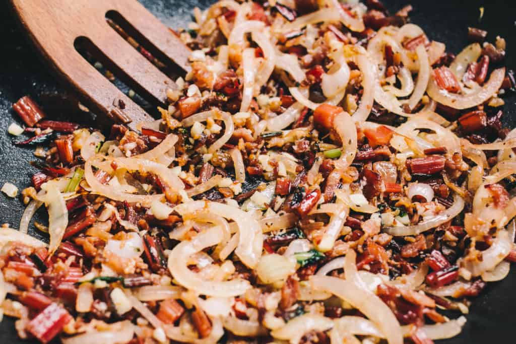 Caramelized onions with bacon in a skillet with a wooden fork