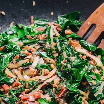 cooked swiss chard in a skillet with onions bacon and a wooden fork
