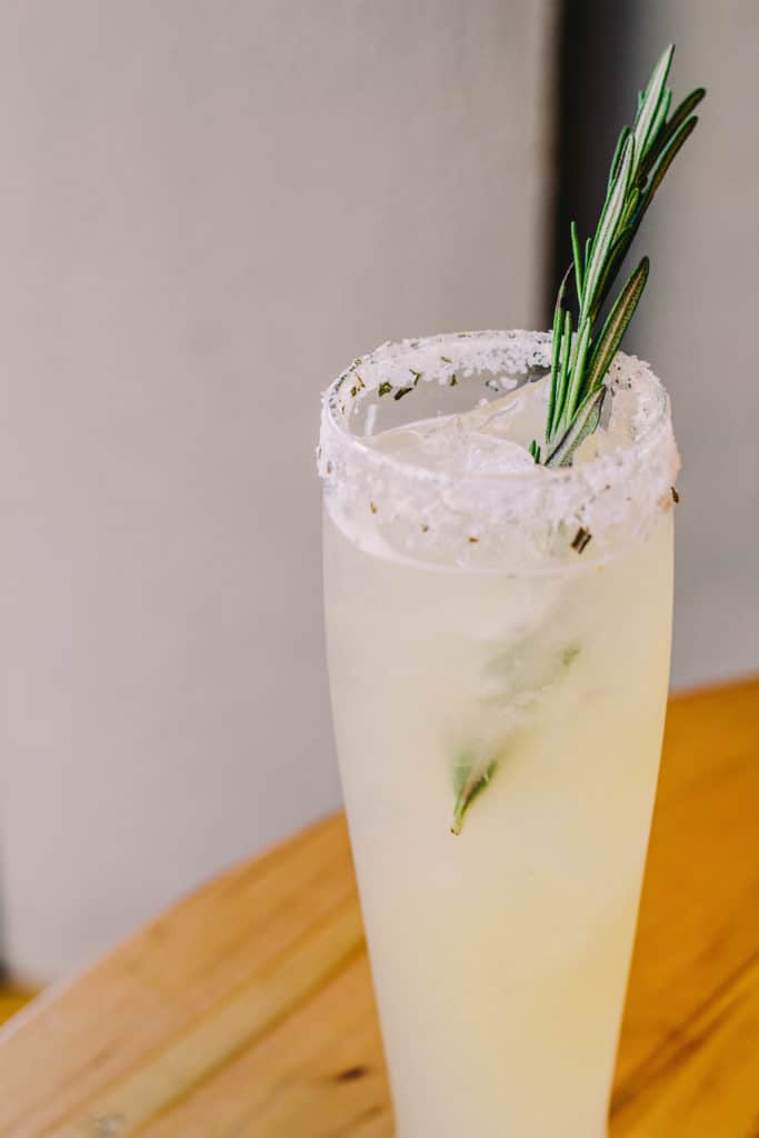 tall cocktail with a salted rim and a sprig of rosemary
