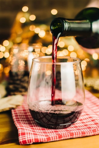 pouring red wine into a glass with twinkling lights in the background