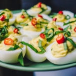 Plate of deviled eggs with thai basil and bird's eye chilis on a green plate