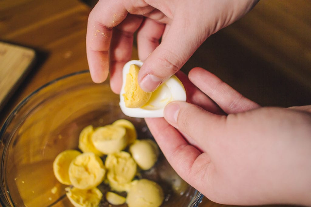 hand removing hard boiled egg yolks into a bowl
