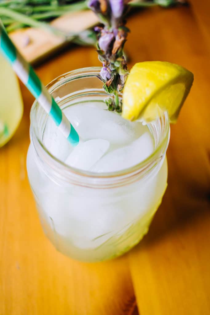 45 degree angle of a mason jar filled with lavender sage lemonade and a white and teal striped paper straw