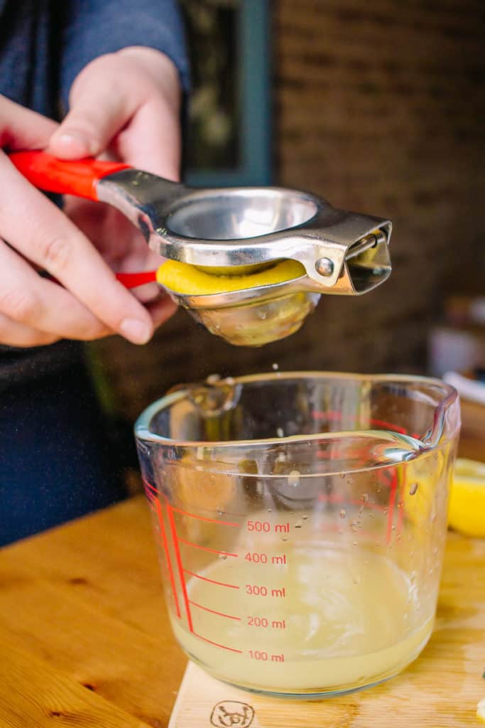 hands squeezing fresh lemon juice into a pitcher using a citrus squeezer