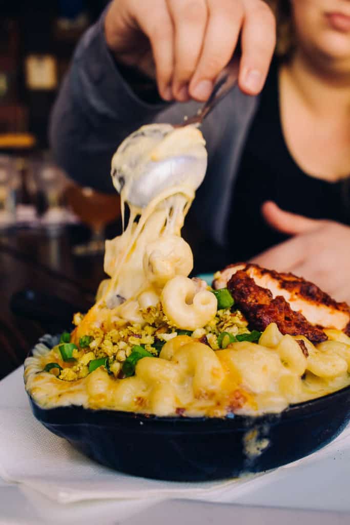 hand stirring up super cheesy mac and cheese topped with fried chicken