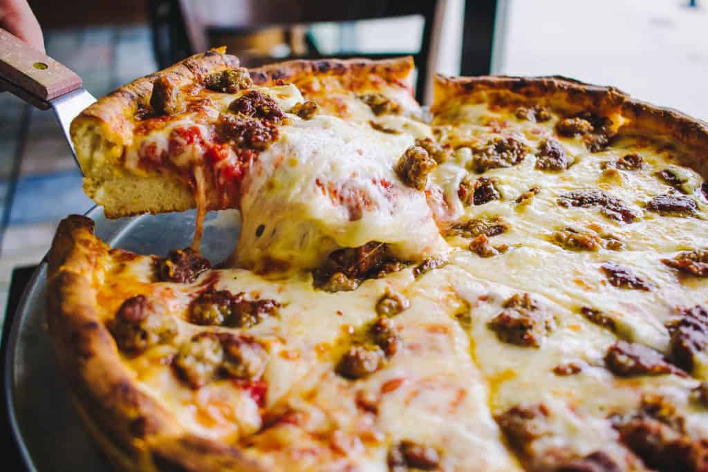 deep dish pizza with italian sausage and a cheese pull