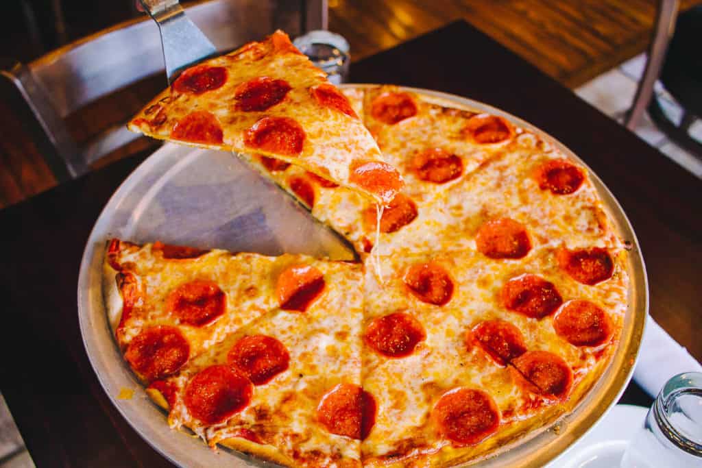 pepperoni thin crust pizza with a slice being lifted