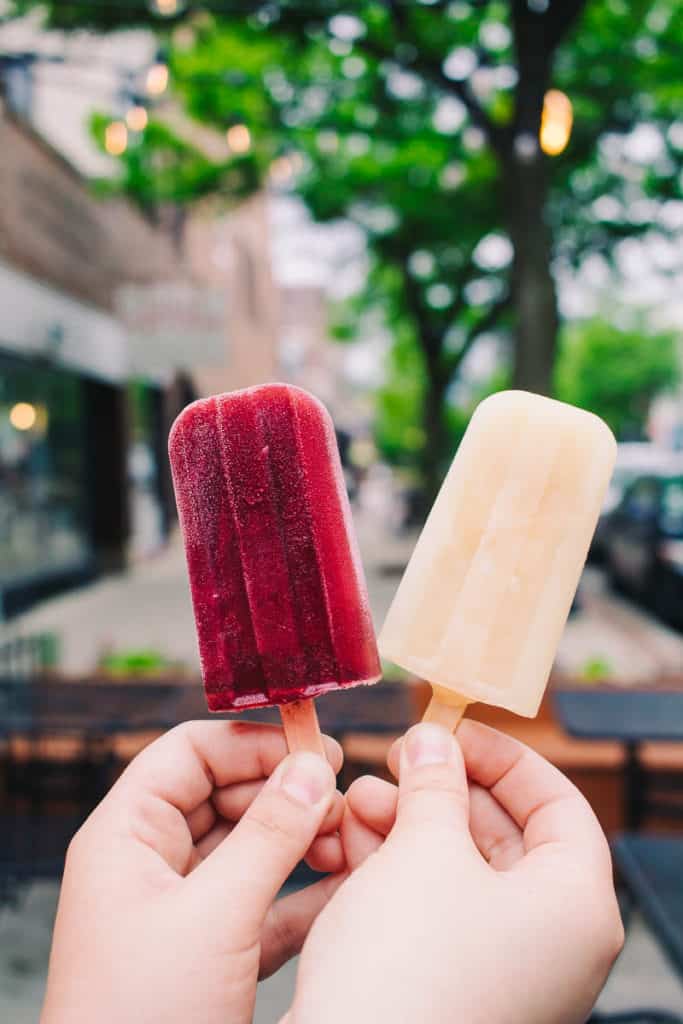hand holding up two popsicles with a tree in the background