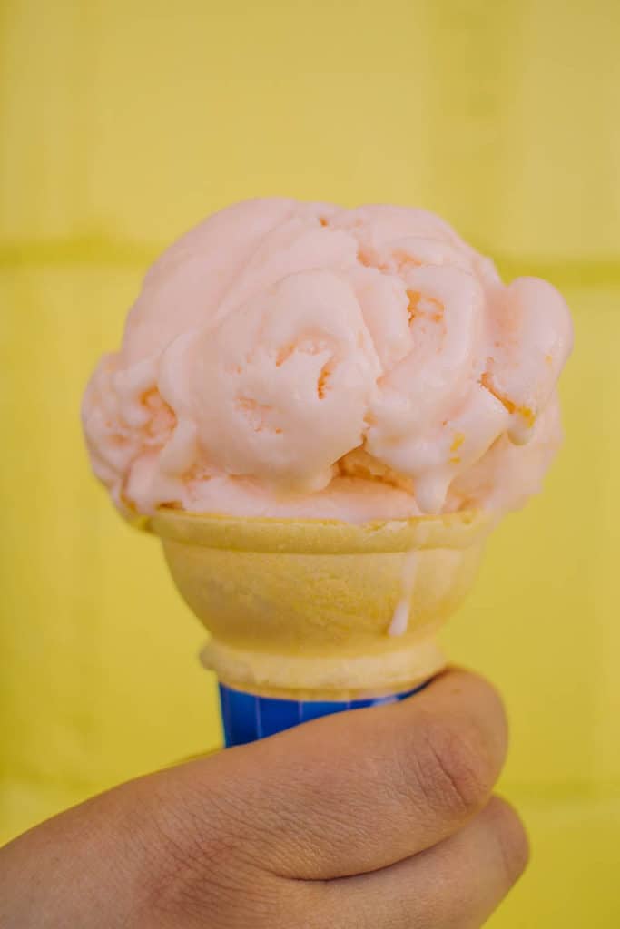 hand holding up a cone of peach frozen yogurt against a yellow wall