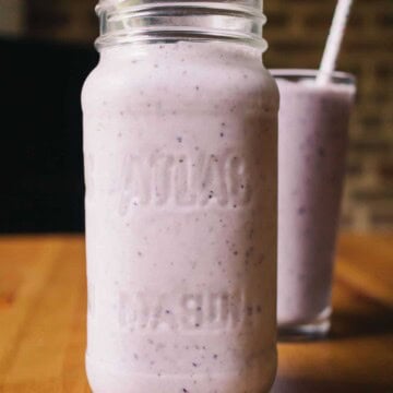 two glass mason jars with low carb blueberry smoothies with two straws