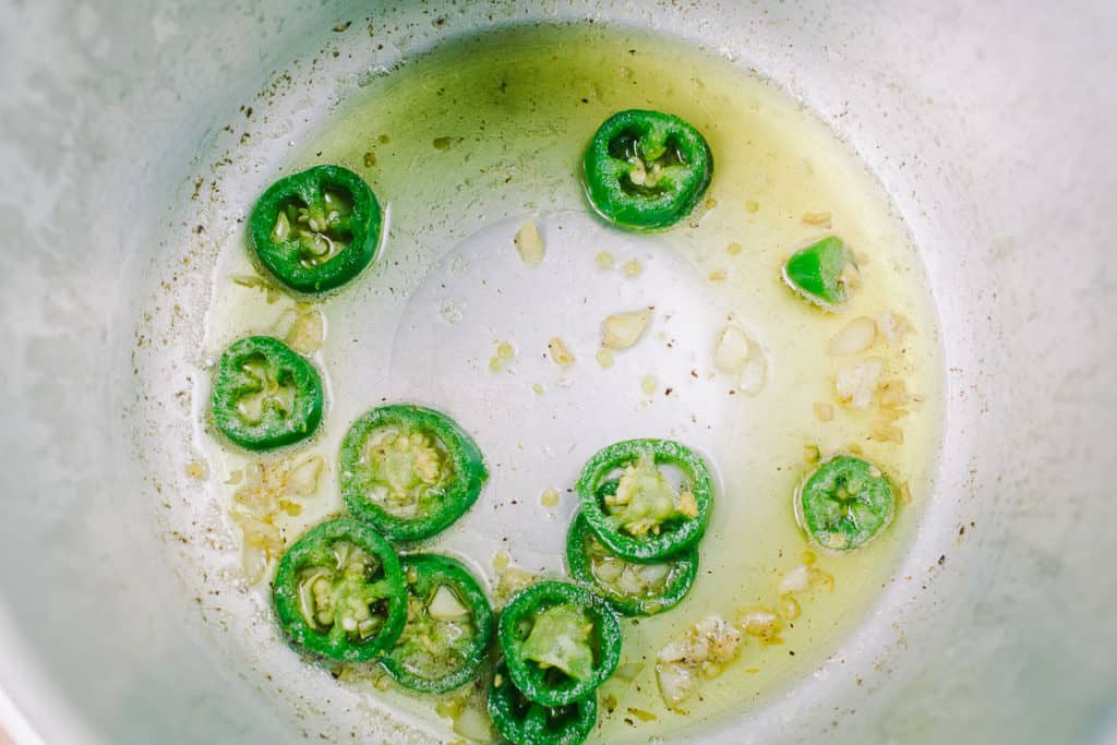 jalapenos and garlic in the bottom of a pressure cooker in oil 