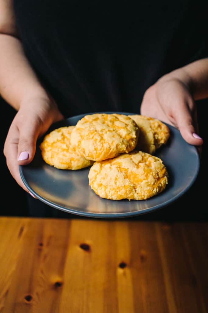 hand coming out of a dark background with a grey plate full of cheddar biscuits