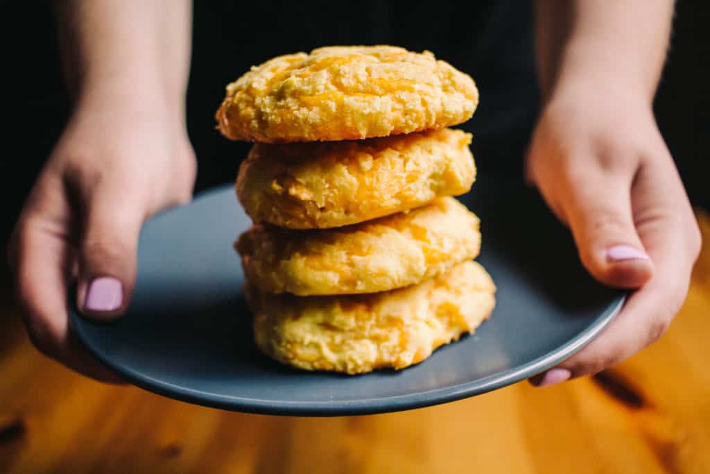 hands holding a plate with a stack of low carb cheddar biscuits