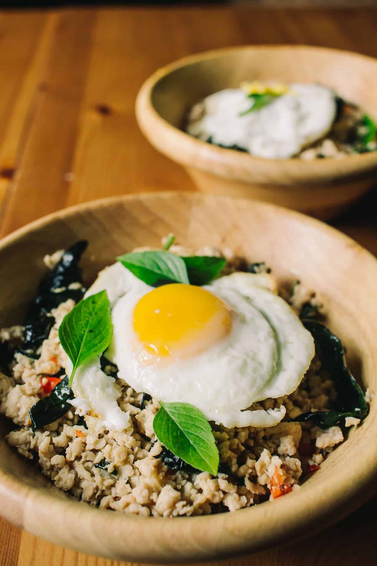 two bamboo bowls with thai basil chicken and fried eggs on top