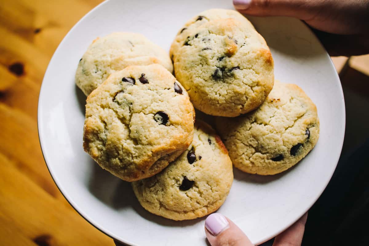 two hands holding a white plate with chocolate chip cookies