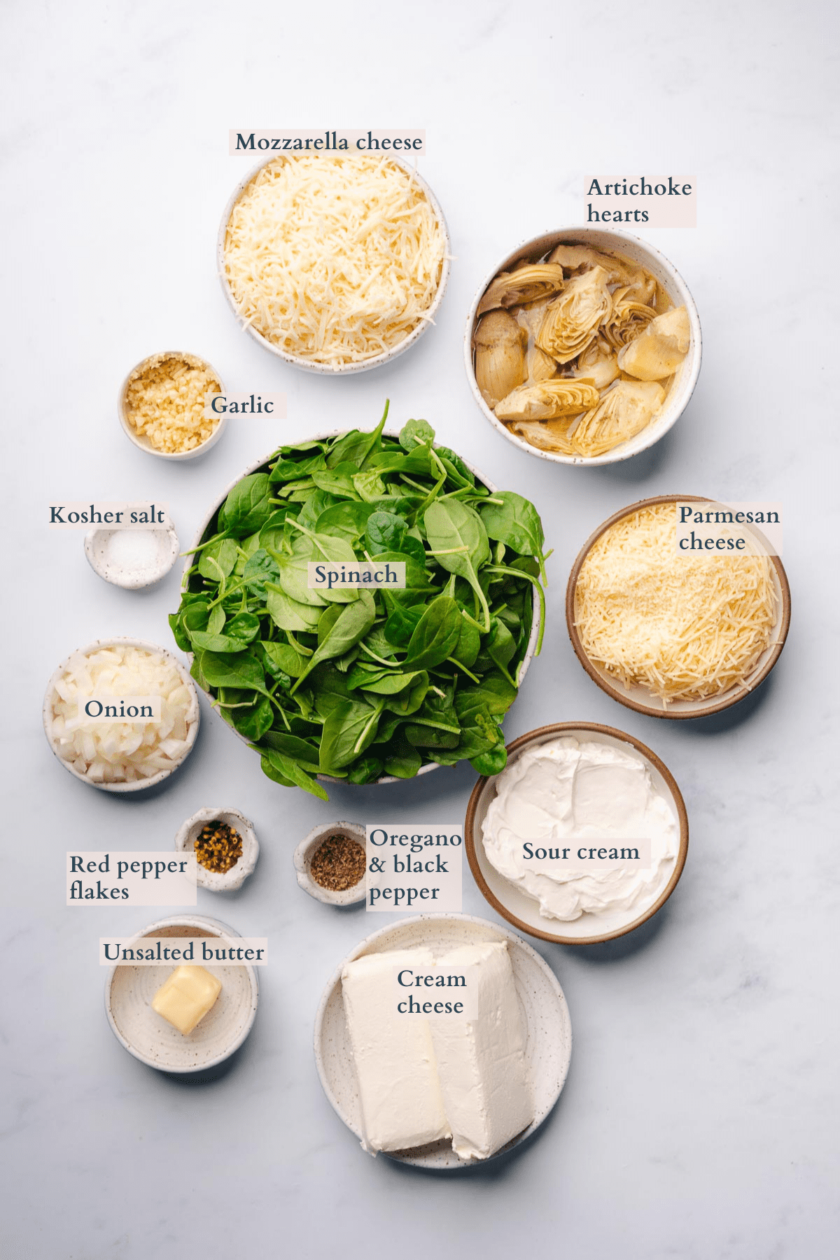 ingredients to make keto spinach artichoke dip in ceramic bowls with text to denote different ingredients