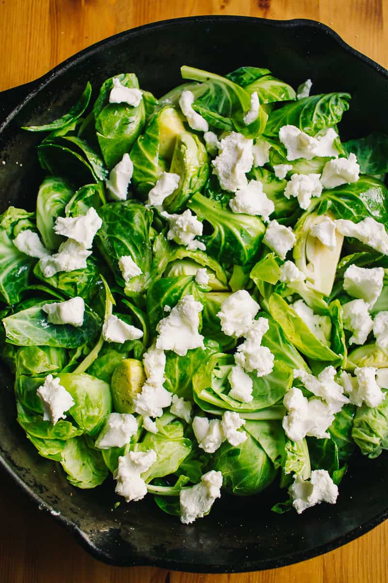 crumbled creamy goat cheese on top of raw brussels sprouts in a cast iron skillet