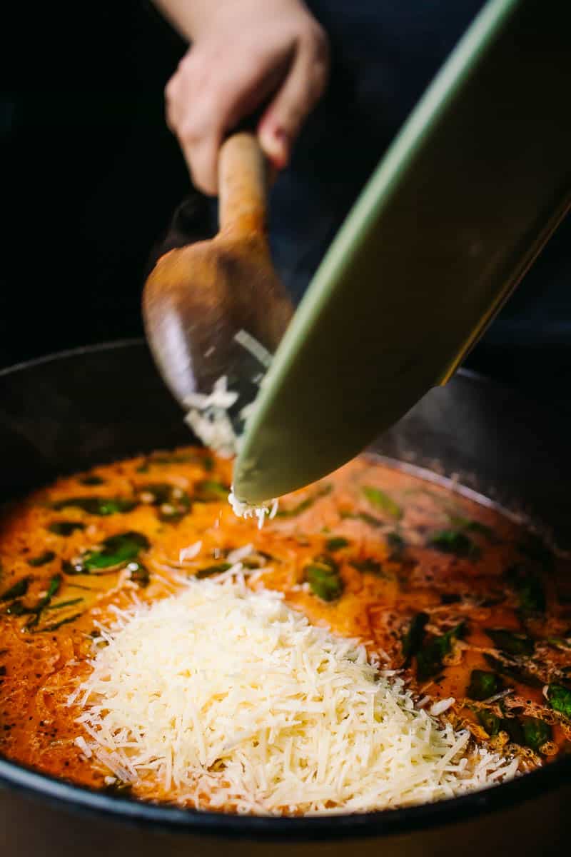 spoon pushing parmesan cheese into lasagna soup broth