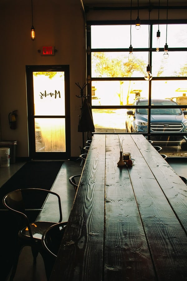 long wooden table inside of a coffee shop looking out to large sunny windows