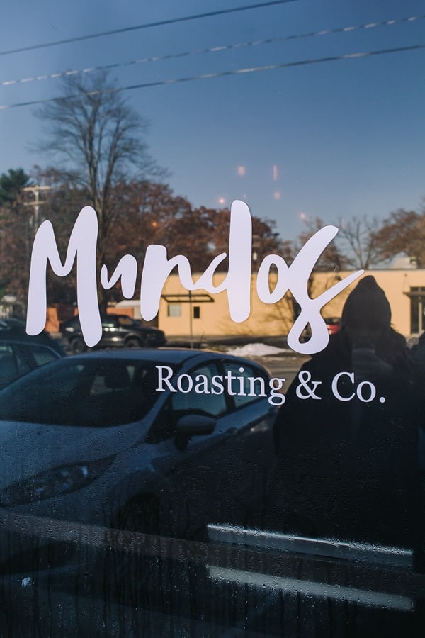 Mundos roasting and co sign on the glass door with a girl in the reflection