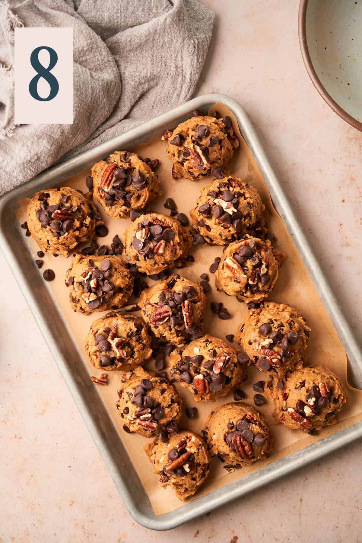 large cookie dough scoops topped with pecan pieces, mini chocolate chips, and large chocolate chips on a small baking sheet. 