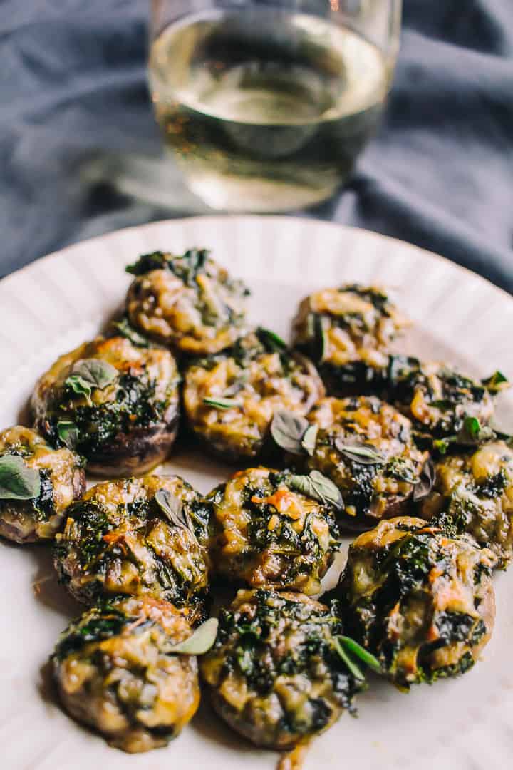 Kale and Mozzarella Stuffed Mushrooms with a grey blue towel in the back and a glass of white wine