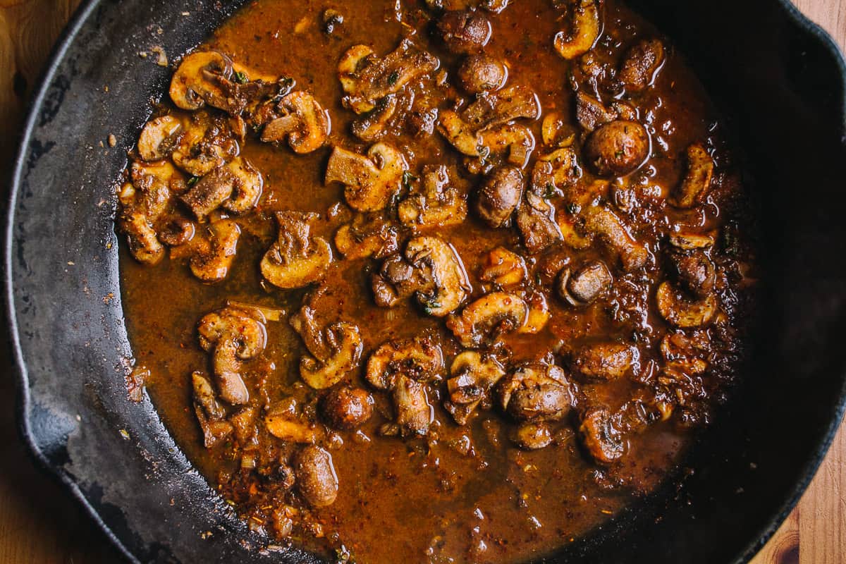 cast iron skillet with mushrooms in a red broth with seasonings