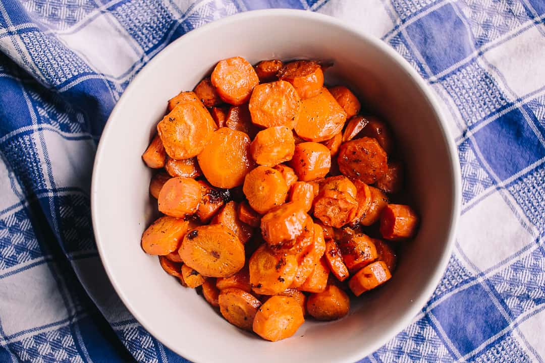 overhead white bowl of roasted carrots with blue and white linen napkin