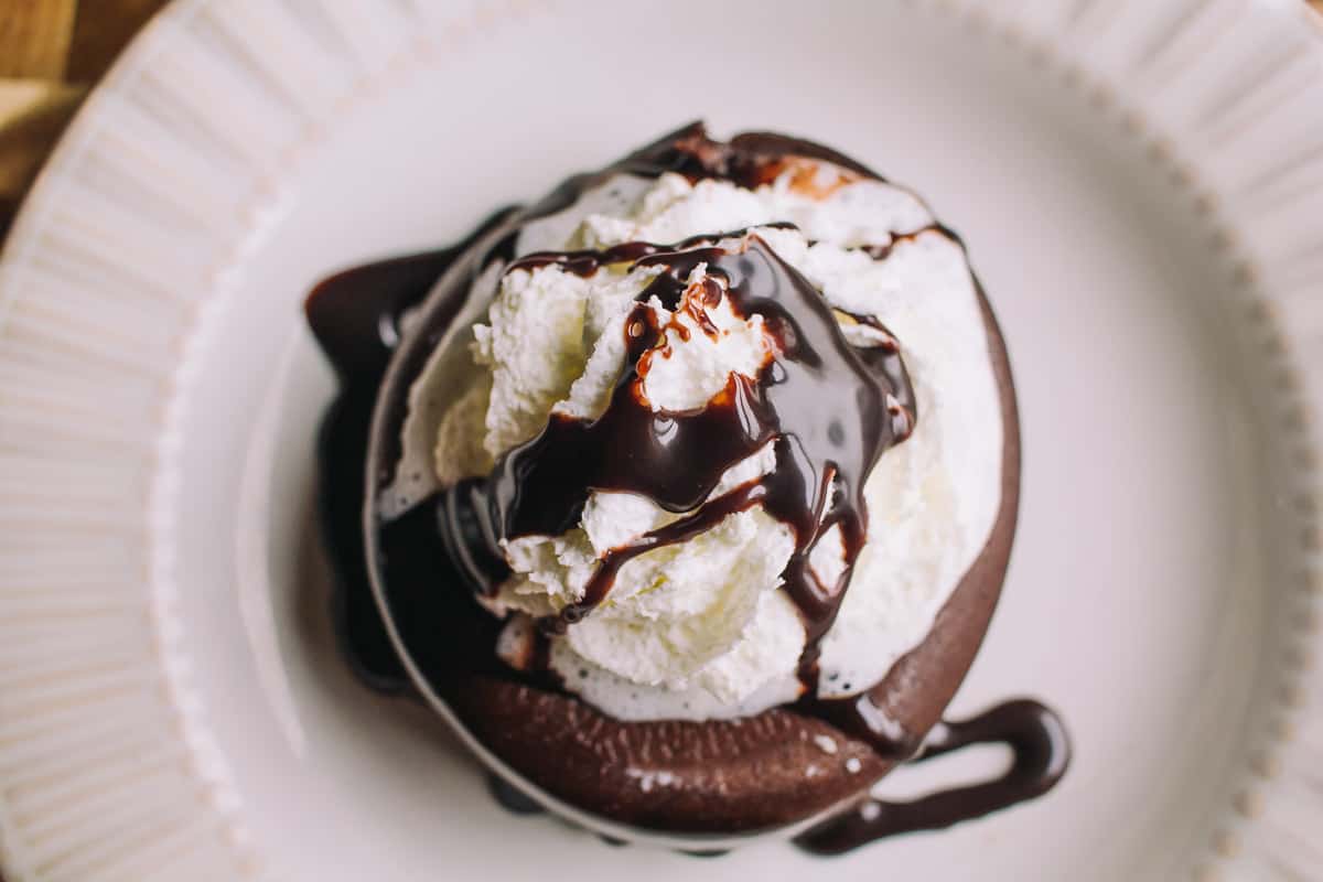 chocolate lava cake on a white plate with whipped cream and chocolate syrup