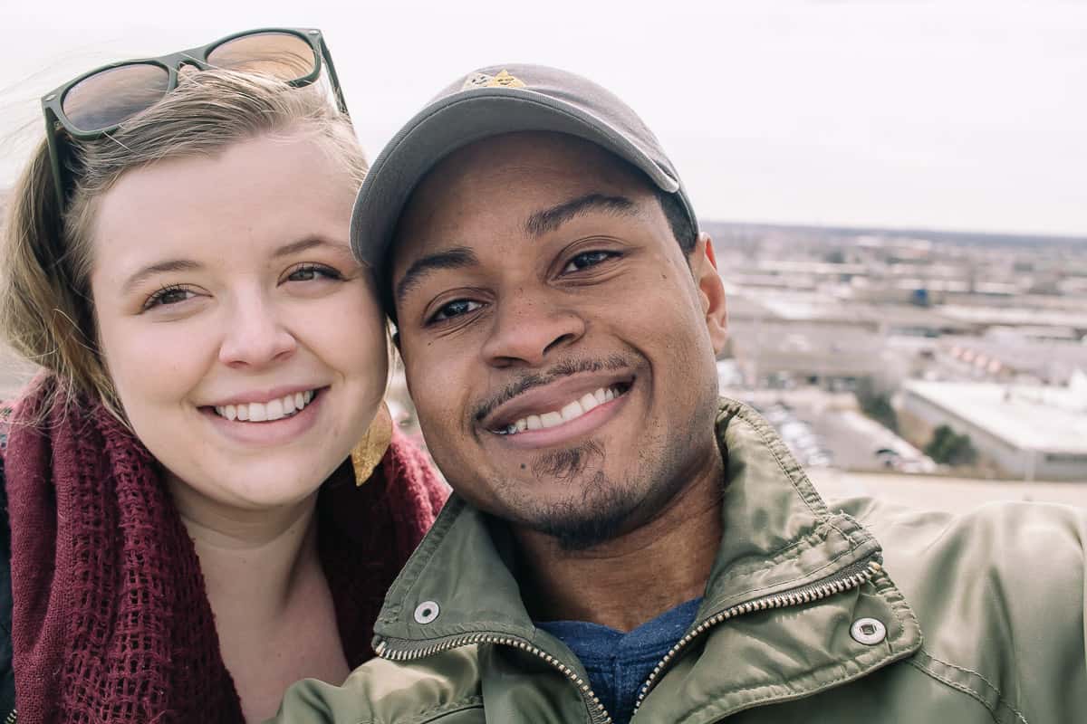 cute couple smiling into the camera with a backdrop of the airport