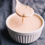 Low Carb Thousand Island Dressing in a white bowl on a grey blue napkin, being held up on a spoon