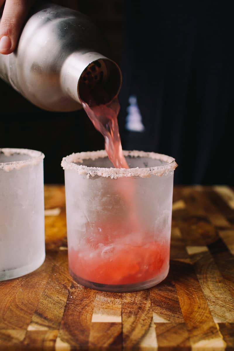 straining blood orange cocktail into a glass
