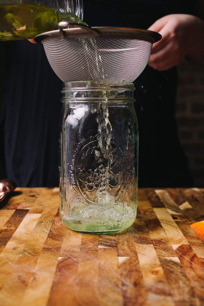 straining serrano infused tequila into a mason jar