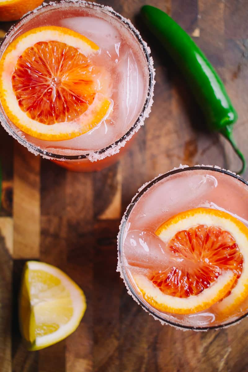 overhead shot of two blood orange cocktails with pink salt and serrano peppers 