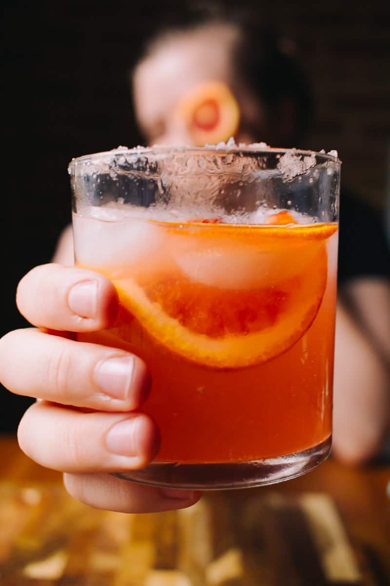 girl holding blood orange cocktail to the camera