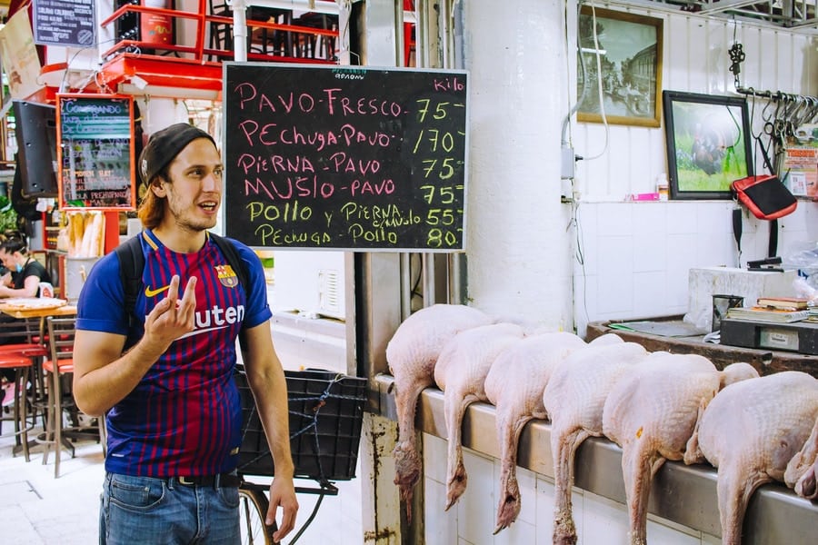 man speaking to a crowd of people in a street food market with a row butchered geese 