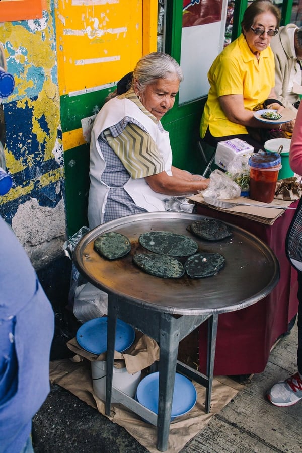woman cooking blue corn tortillas at a street food stall in mexico city
