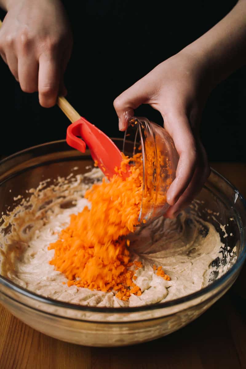 hand Adding shredded carrots to a cupcake batter with a rubber spatula