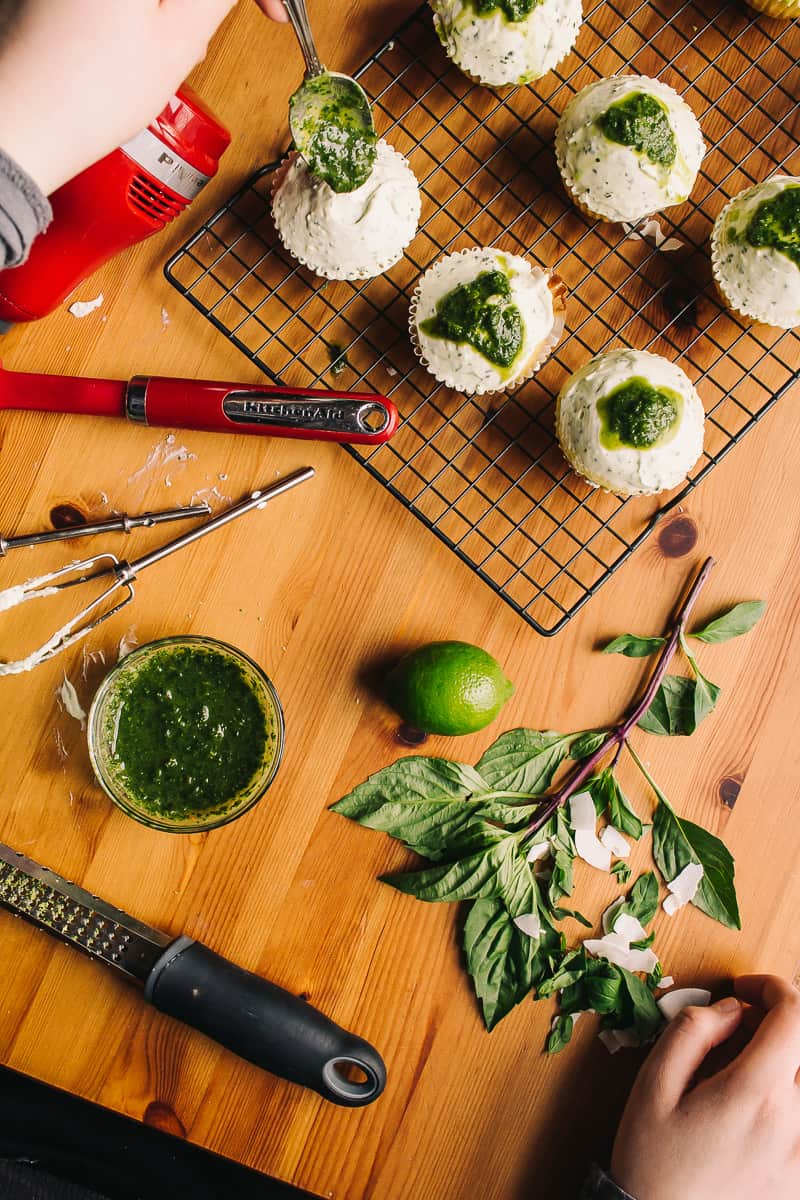 overhead view of making Low Carb Thai Basil Lime and Coconut Cupcakes with fresh ingredients and a lovely mess of kitchen tools, cupcakes and cooling racks