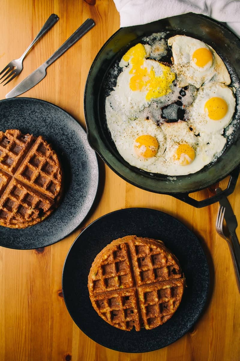overhead view of crispy waffles with a cast iron skillet of sunny side up eggs